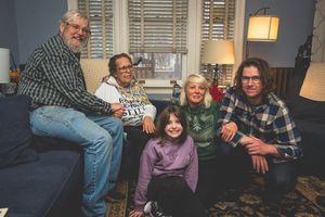A group of people, including an older man and woman, sitting together on a couch in a cozy living room setting.