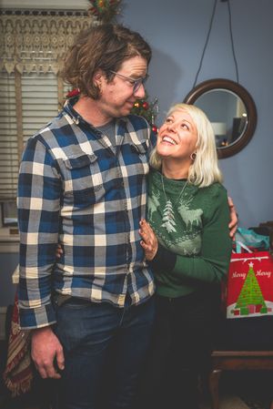 A smiling couple embracing in a cozy room decorated for the holidays.