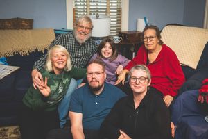 A group of smiling people sitting together on a couch in a living room.