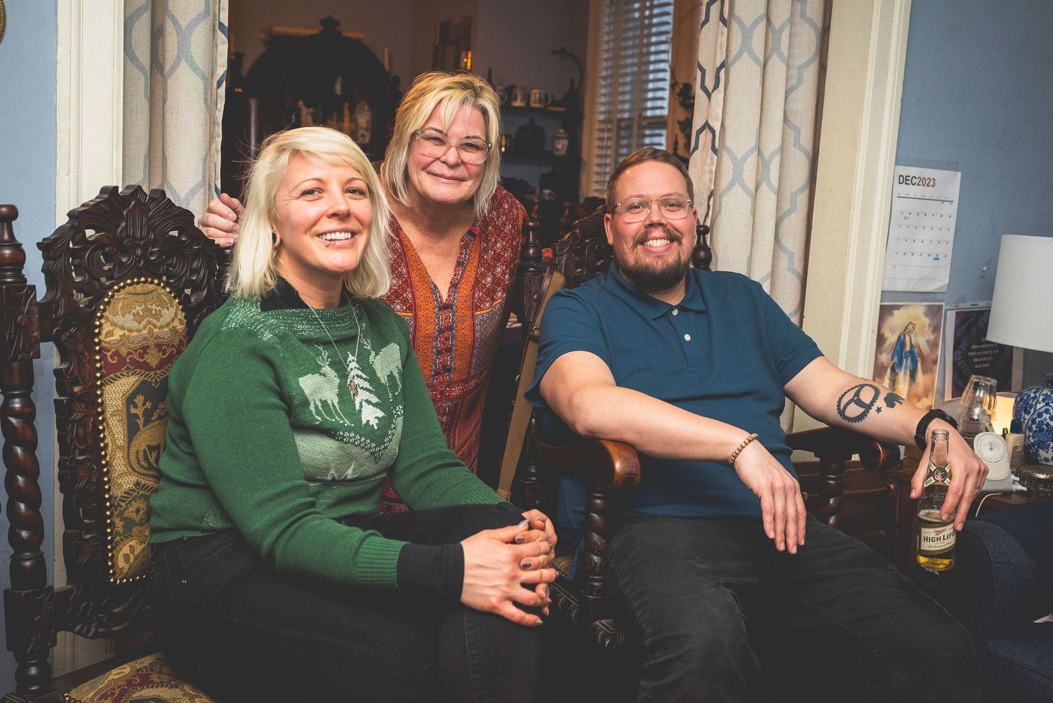 Three people, two women and one man, stand together smiling in a room with ornate furnishings.
