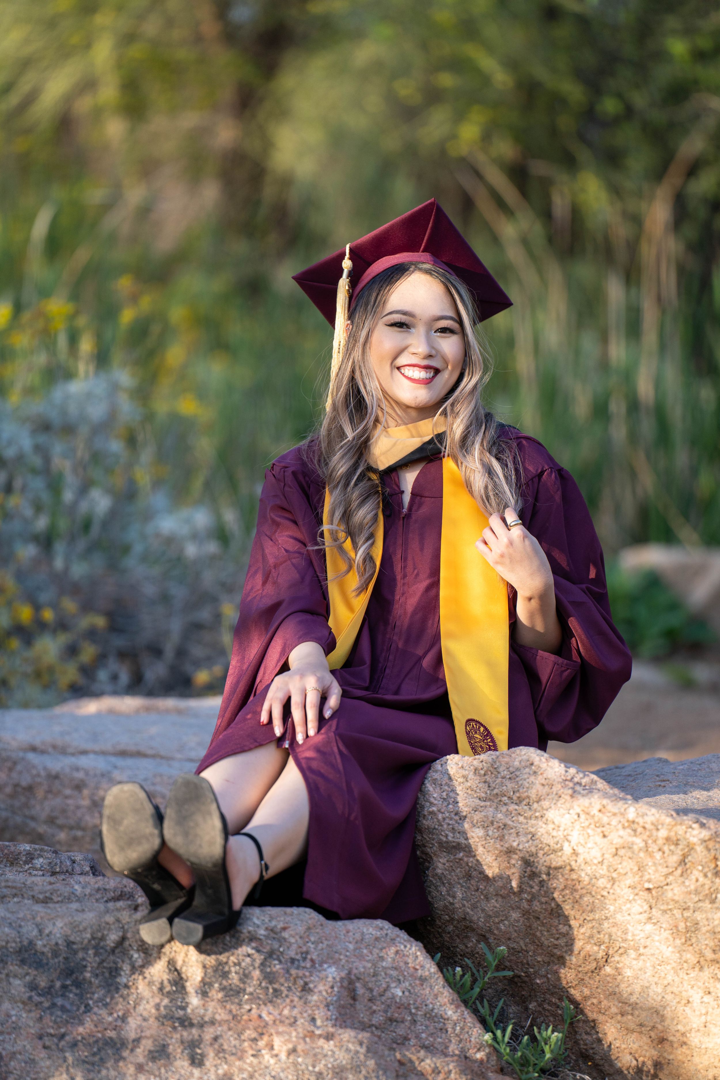 ASU graduate sitting cross-legged on rocks during a golden hour photoshoot in Tempe, photographed by N&D Media Production.