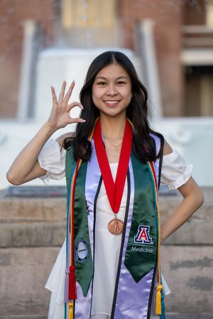 U of A graduate in a white dress throwing the Bear Down sign at Old Main Fountain in Tucson, captured by N&D Media Production.