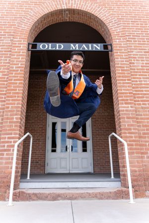 Graduation student leaping mid-air in a Spider-Man pose in front of Old Main at UofA, photographed by N&D Media Production.