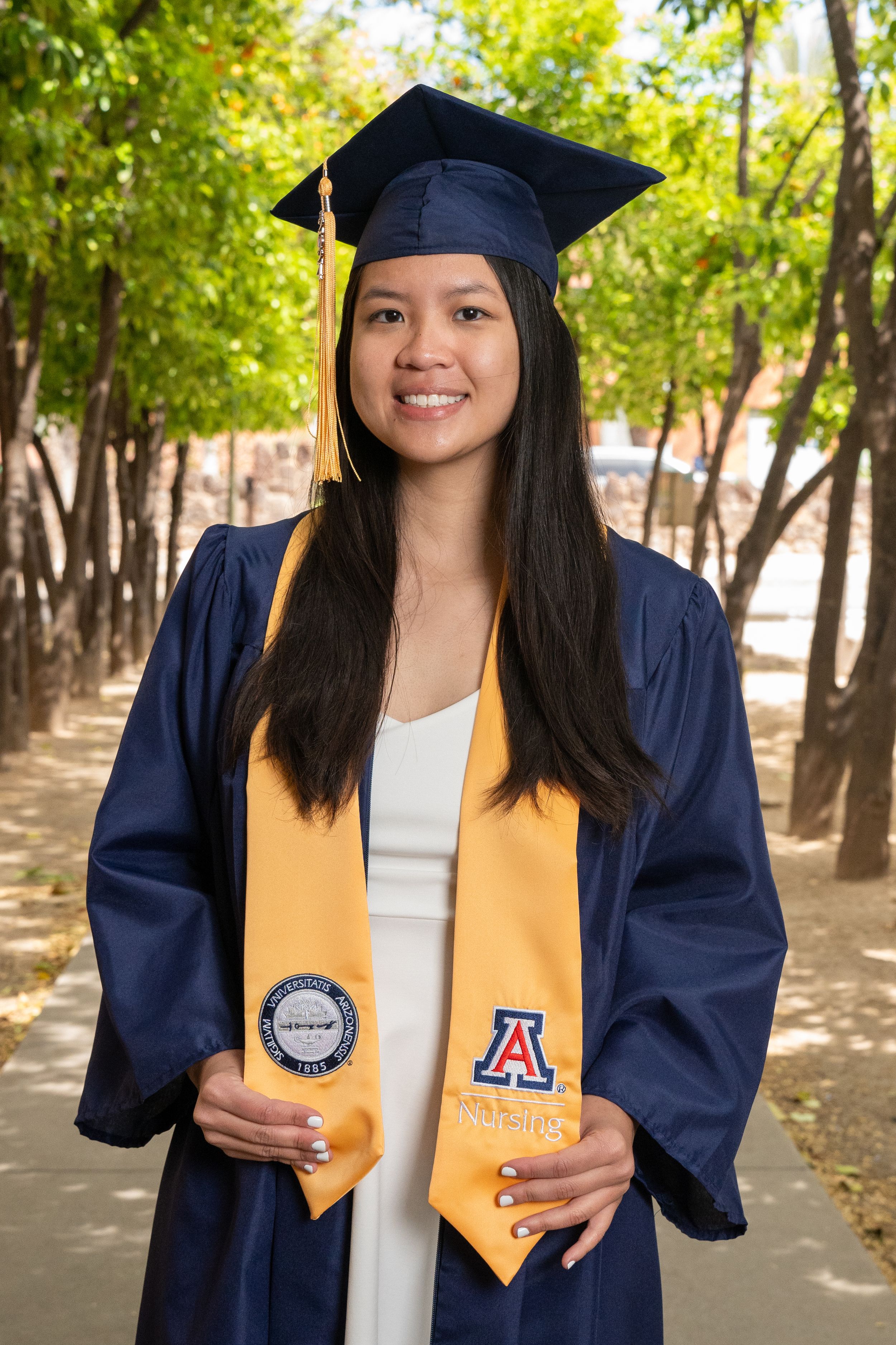 Nursing senior posing with her graduation stole along the scenic orange grove path at UofA, photographed by N&D Media Production.