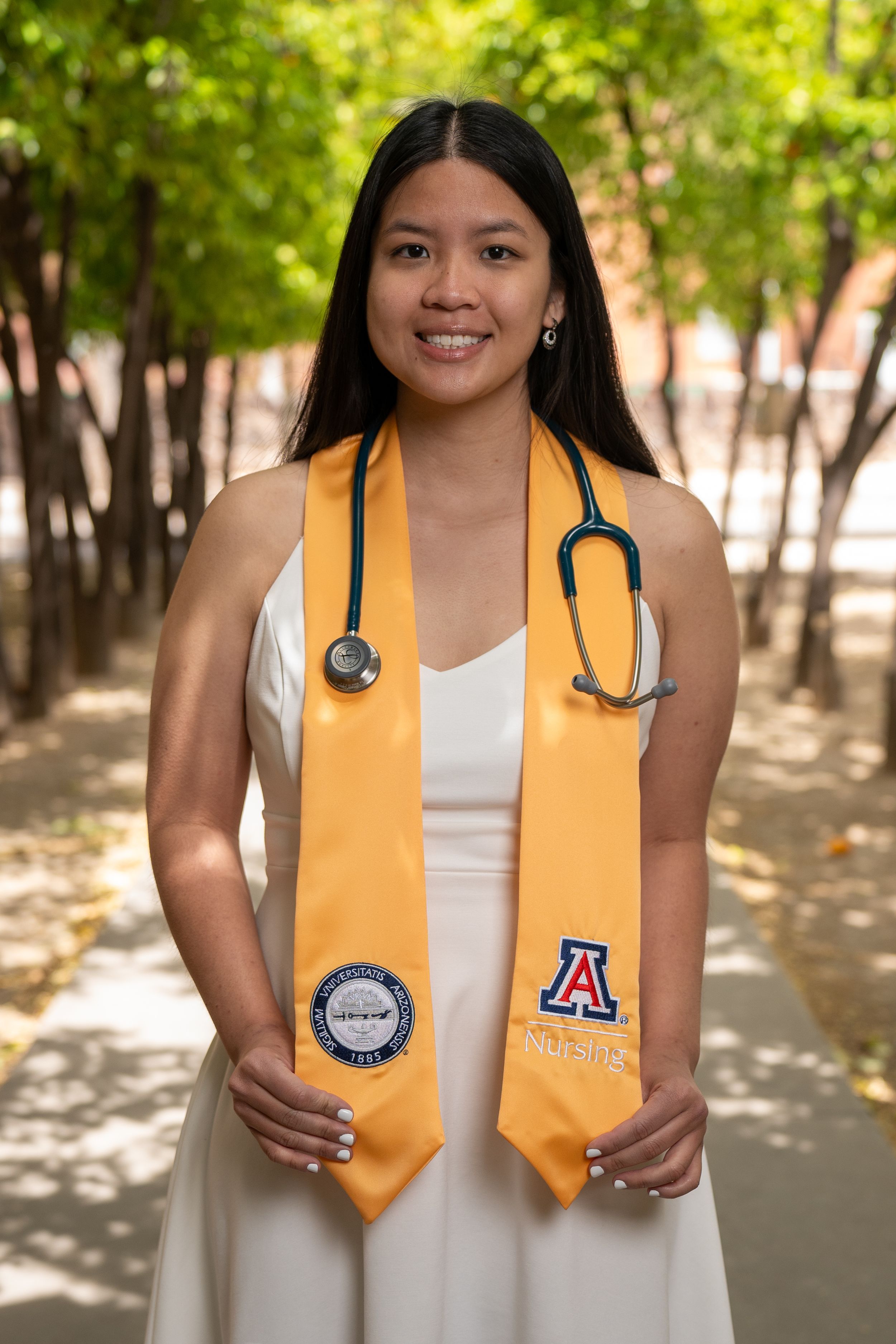 Nursing graduate with stethoscope posing along the University of Arizona orange grove path, captured by N&D Media Production.