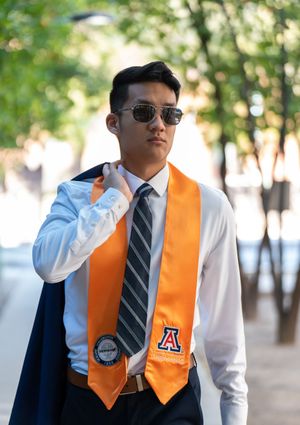 UofA engineering graduate walking through an orange grove holding his gown over his shoulder, captured by N&D Media Production.