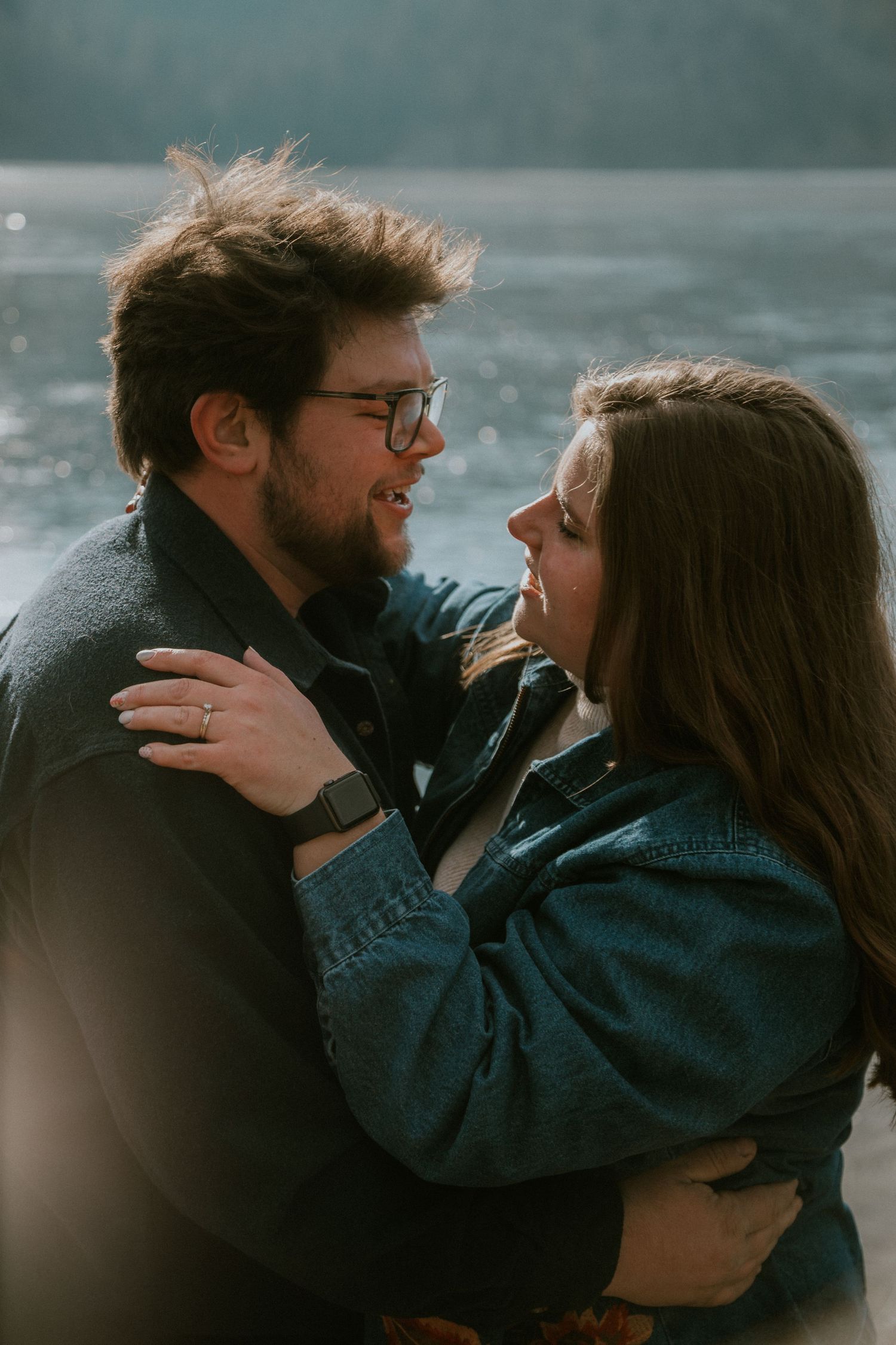 A bearded man and a woman embrace affectionately while standing in front of a body of water.
