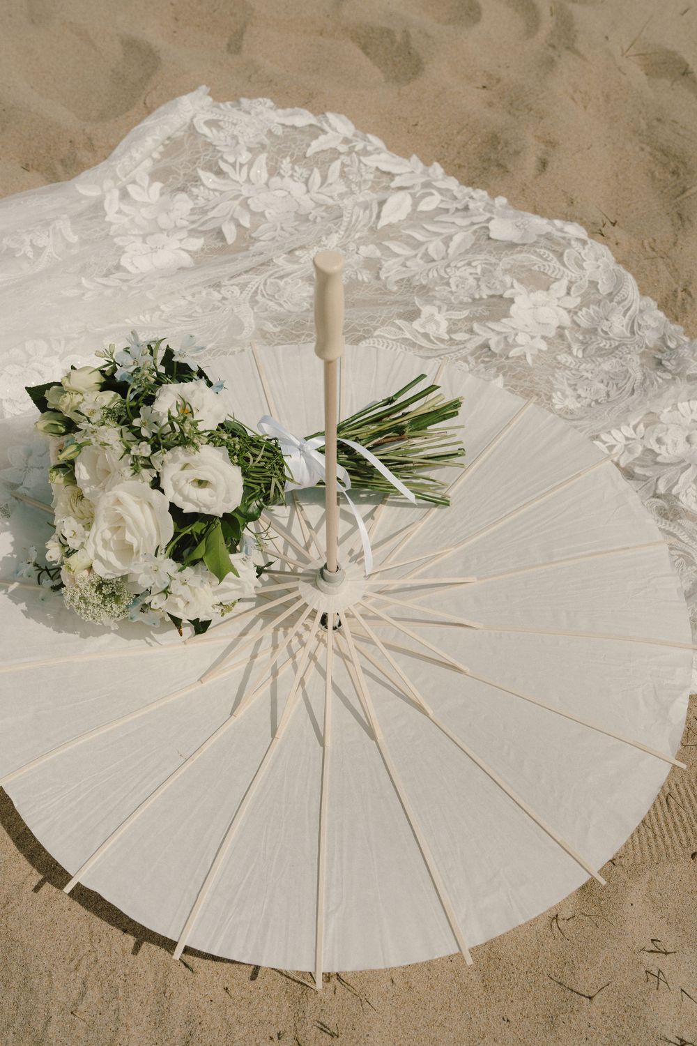 White paper parasol decorated with delicate floral arrangements and greenery on a sandy beach setting.