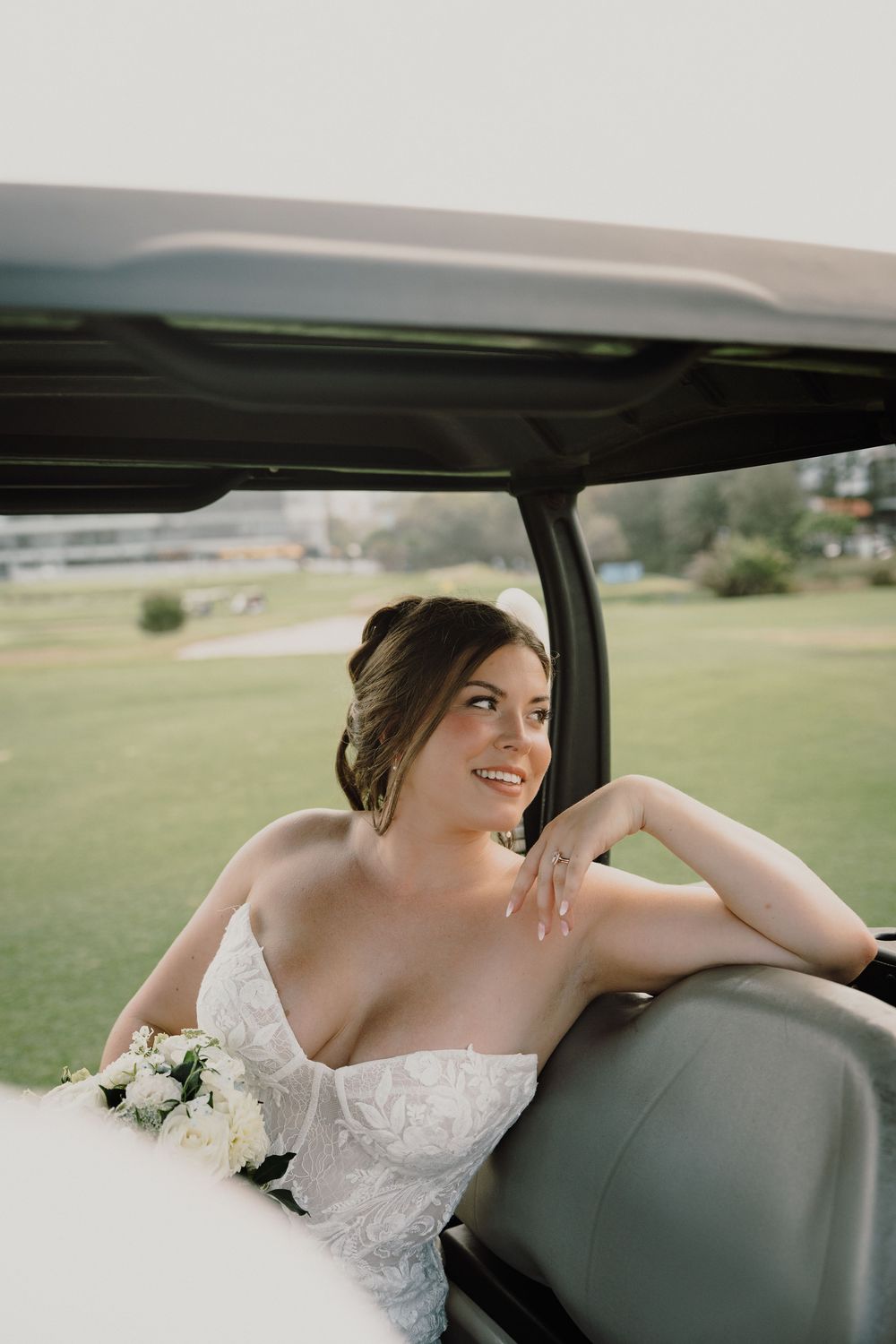 A person in a white lace wedding dress sits in a car looking out the window on their special day.