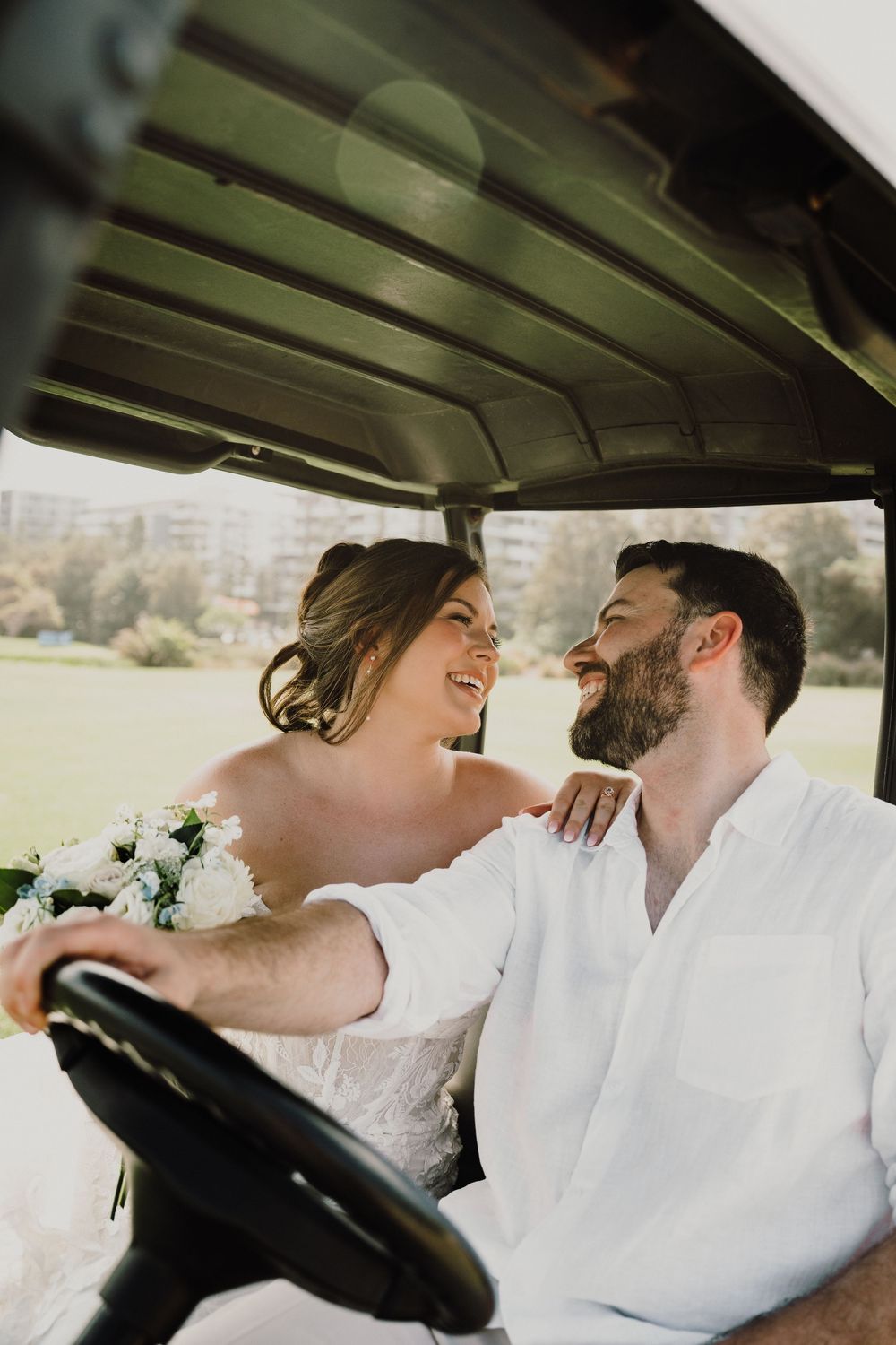 A happy couple shares a joyful moment while sitting in a golf cart on their wedding day.