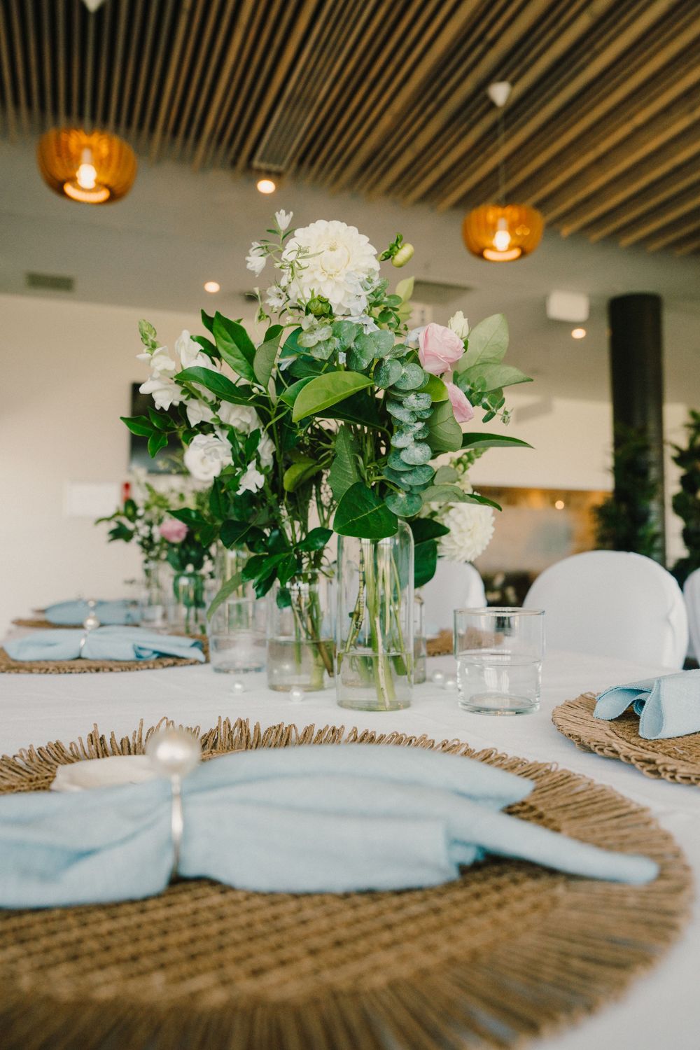 Elegant wedding table centerpieces with fresh greenery and flowers arranged on natural burlap table runners.