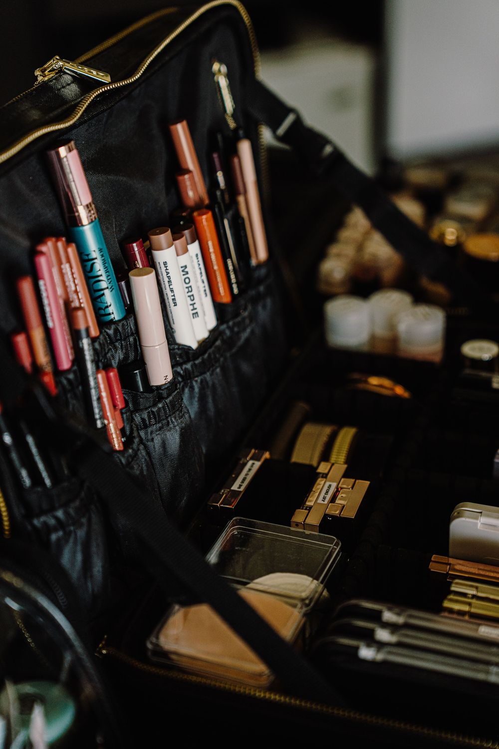 Close-up view of professional makeup brushes and cosmetics organized in a black case under dim lighting.