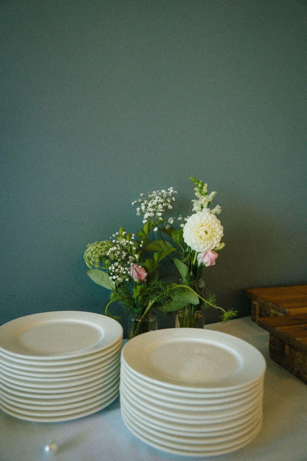A sequence of stacked white plates with delicate flowers and greenery arranged beside them on a dark surface.