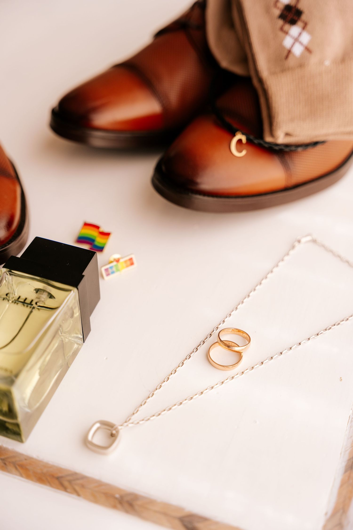 Brown leather dress shoes and wedding rings arranged artistically with ribbons and decorative elements.