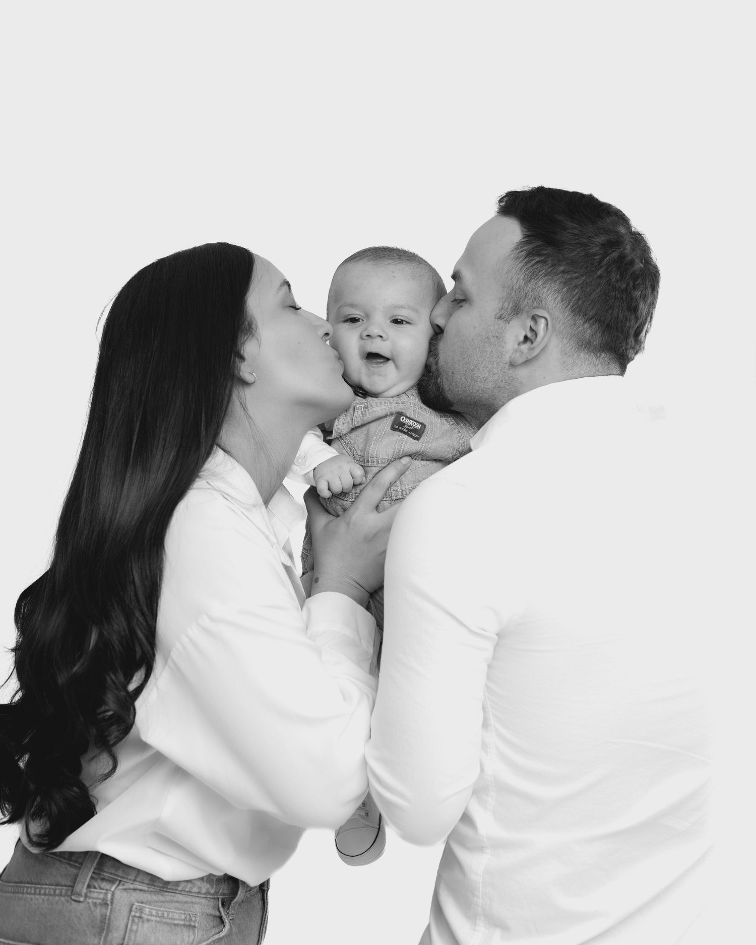 A sweet family moment captured in black and white as parents share loving kisses with their baby.