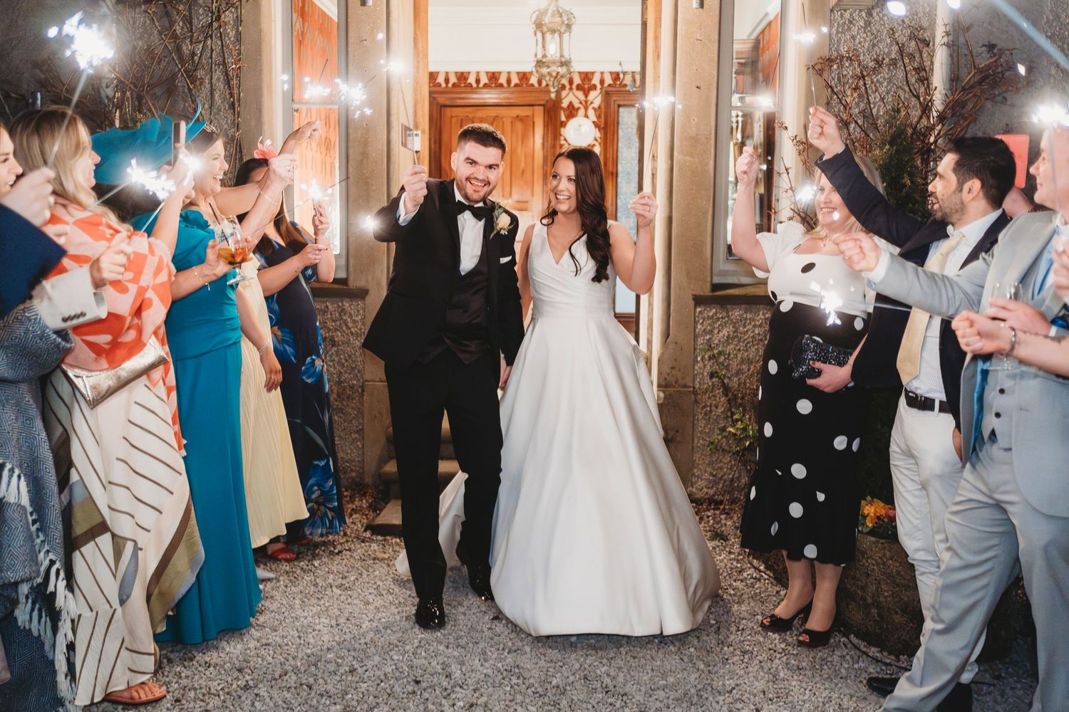 Bride and groom walking through sparkler exit at elegant West Wales wedding venue surrounded by guests