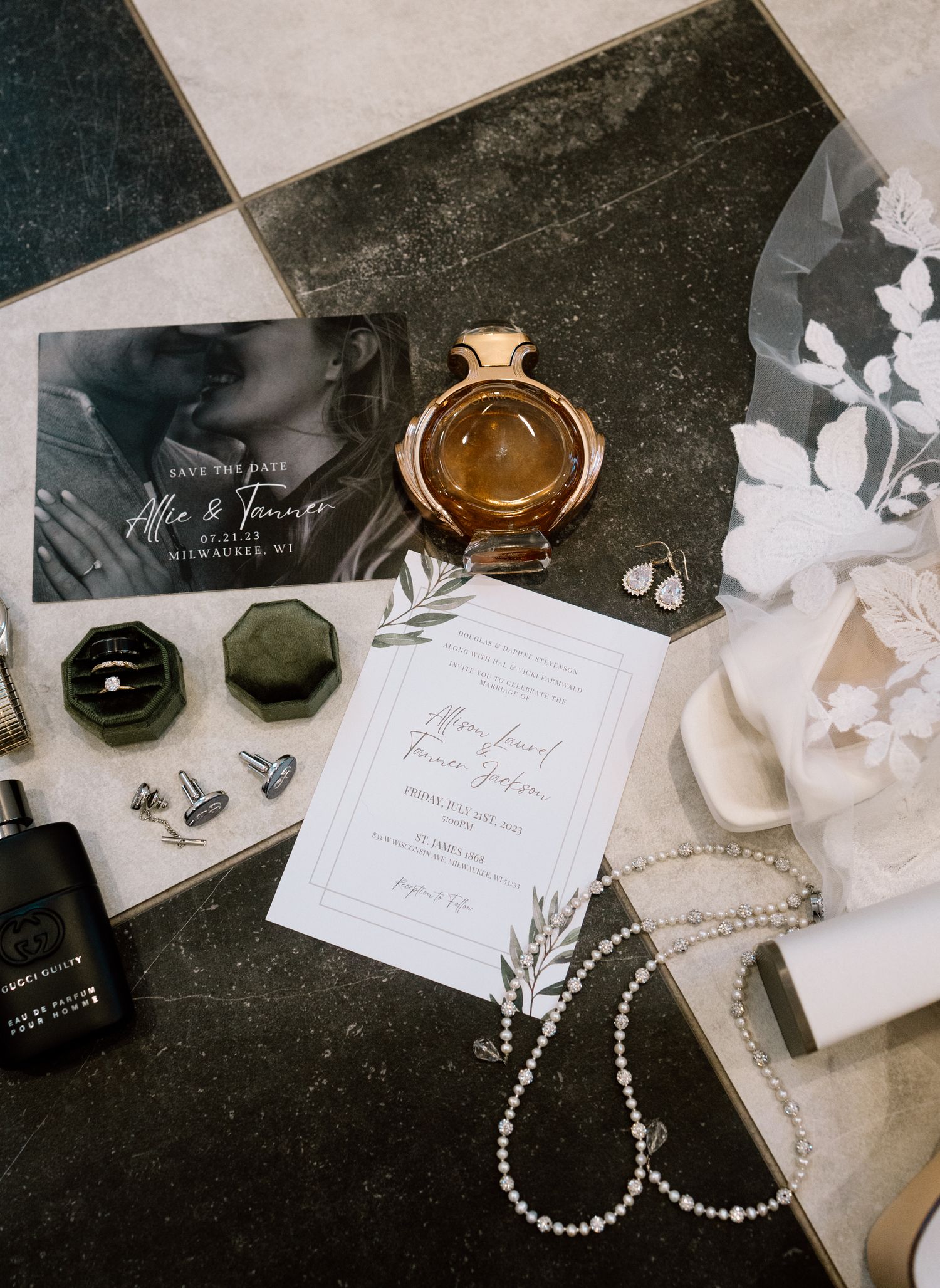 Elegant wedding flat lay with save the date card, perfume, velvet ring box, cufflinks, pearl necklace, and bridal veil on tile.