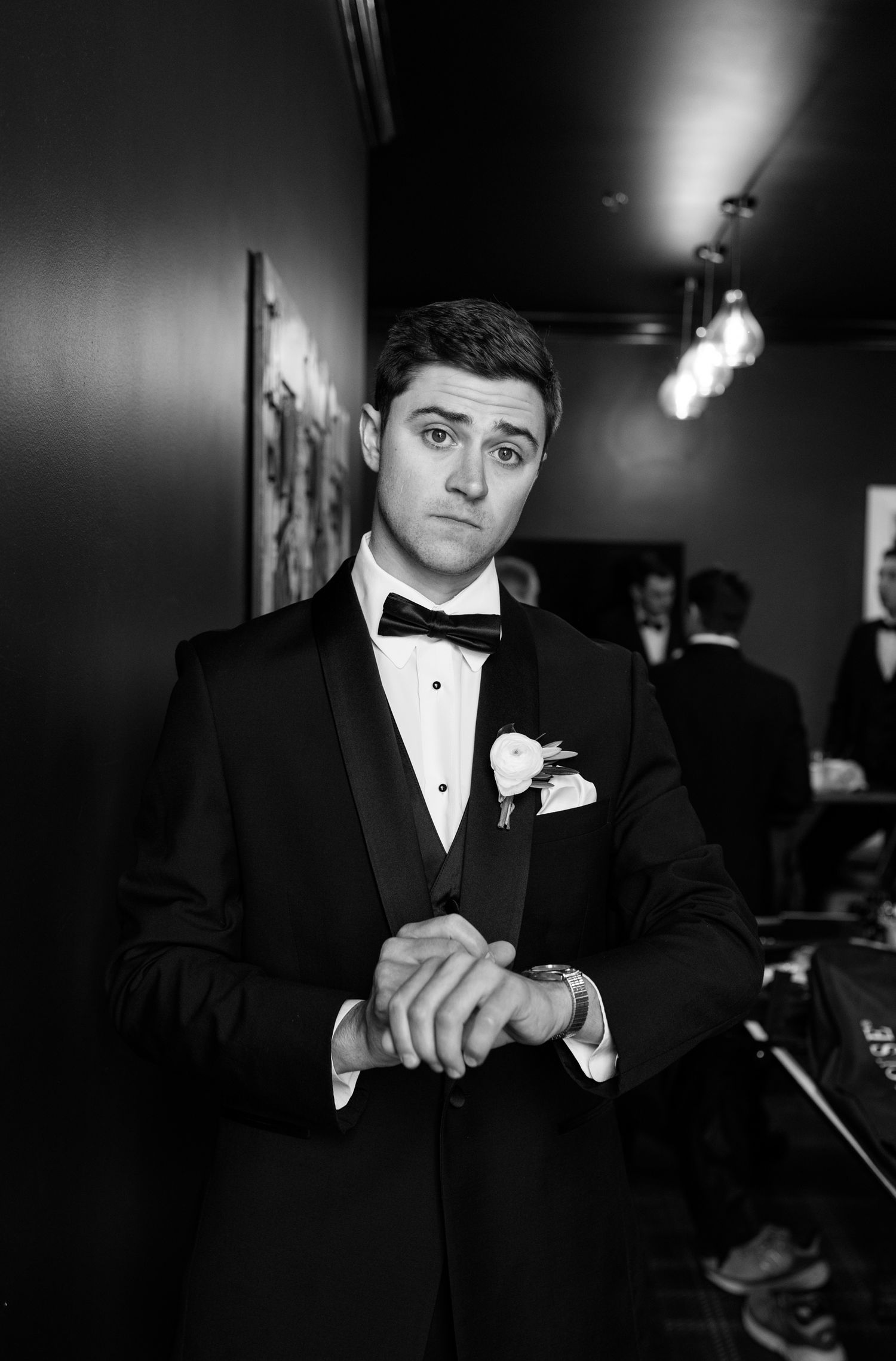Dapper groom in black tuxedo with bow tie and boutonniere adjusting cufflinks before wedding ceremony.