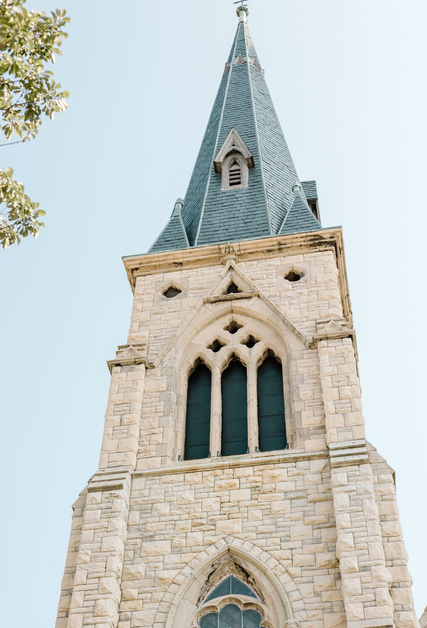 Gothic stone church steeple with pointed spire and arched stained glass windows against clear blue sky.