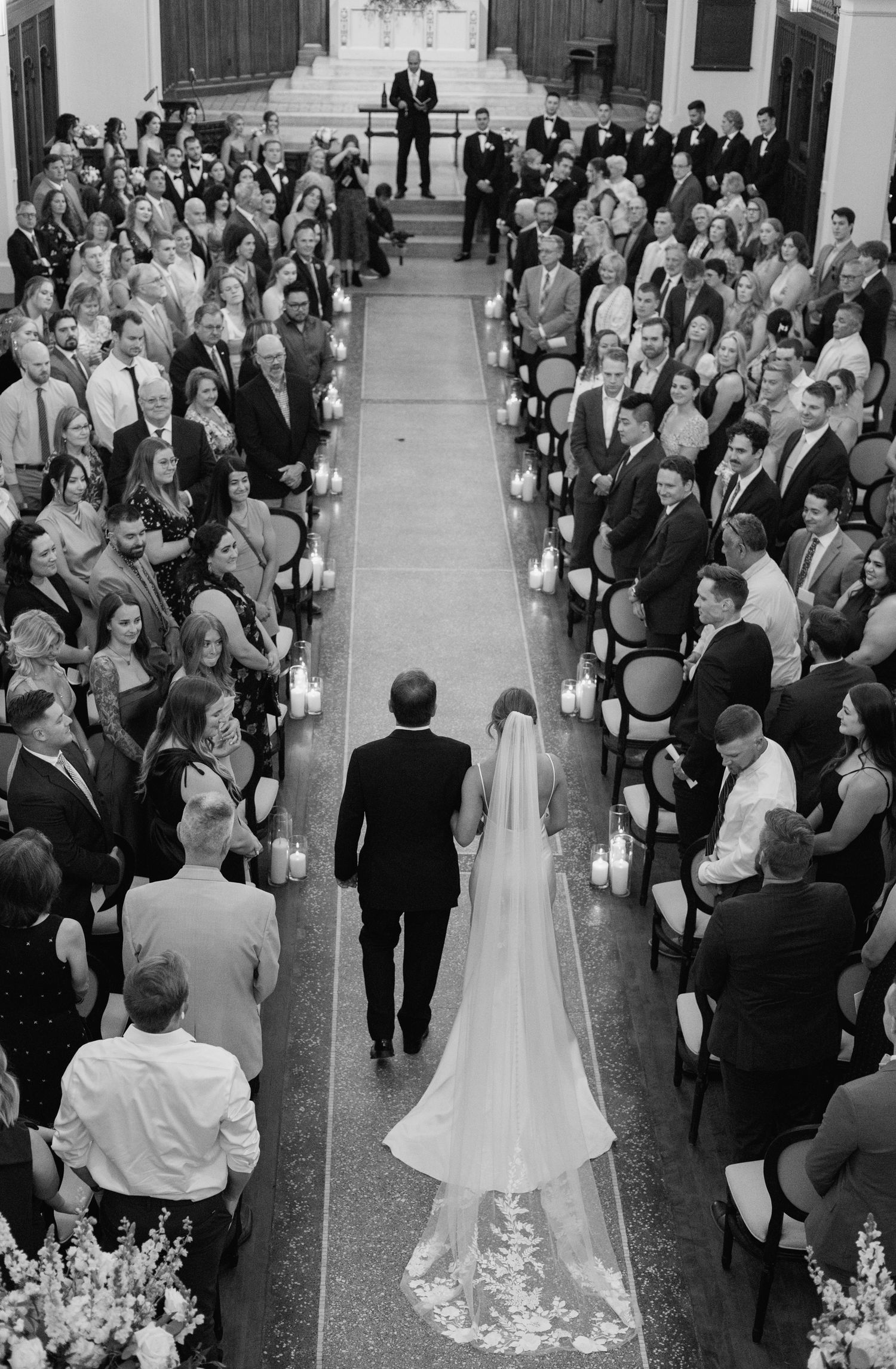 Black and white aerial view of a bride walking down the aisle with her father at a elegant church wedding ceremony.