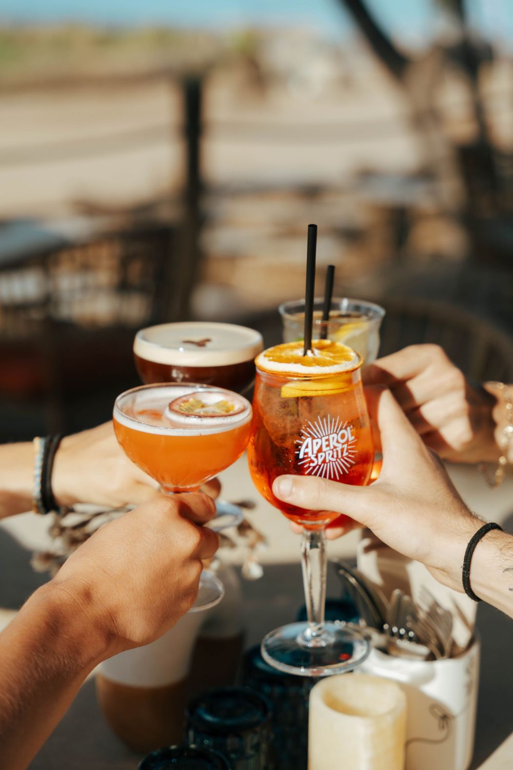 Des amis trinquent à l'Aperol Spritz et des cocktails sur une terrasse extérieure ensoleillée.
