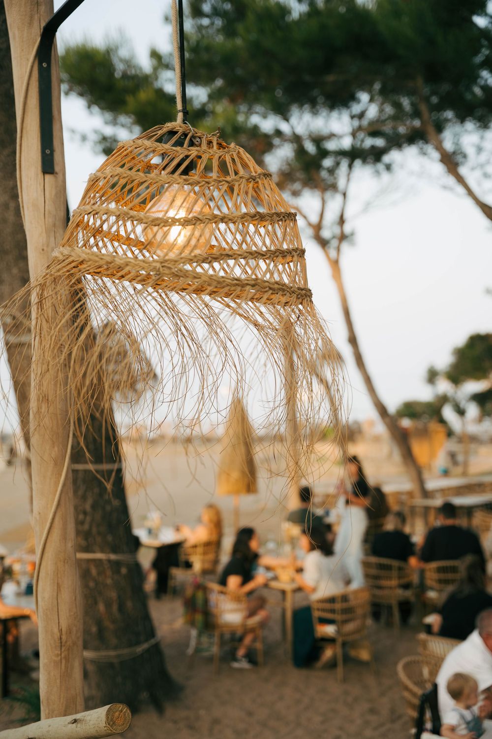 Suspension en rotin tissé suspendue à l'extérieur dans un restaurant en bord de mer avec des convives assis parmi les arbres.