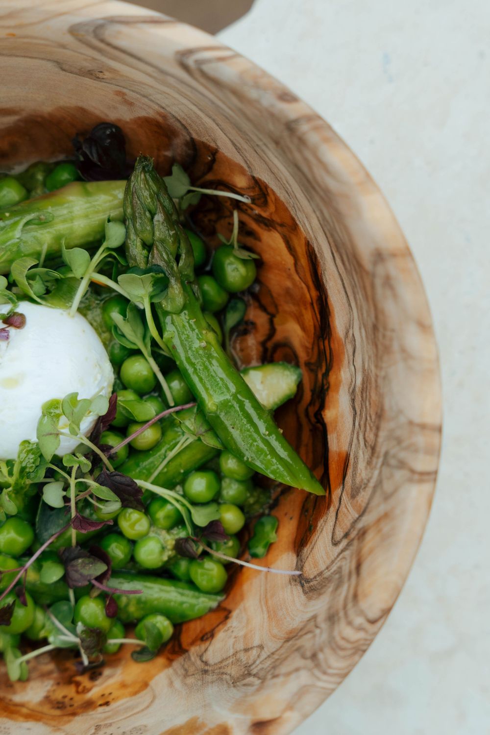 Salade de pois verts frais et d'asperges avec du fromage burrata servie dans un bol en bois rustique.