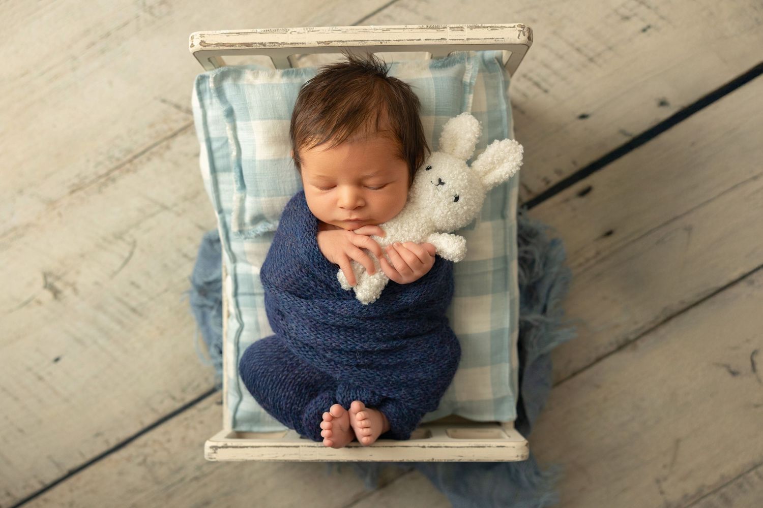 Newborn baby sleeping peacefully in a rustic wooden hanging basket against white wooden floor.
