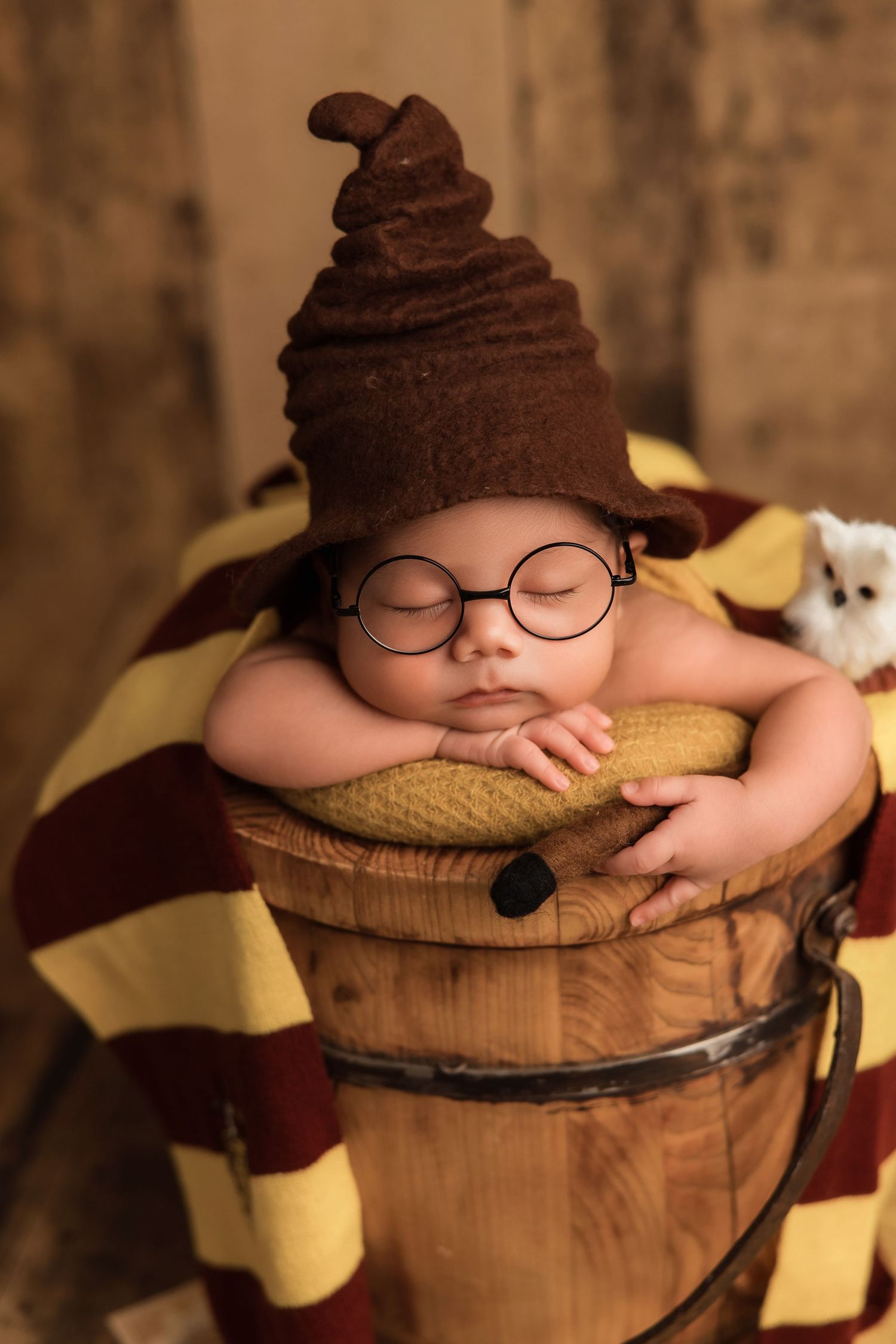 A sleeping baby wearing a brown knit hat rests peacefully on a wooden barrel in a creative newborn photo session.