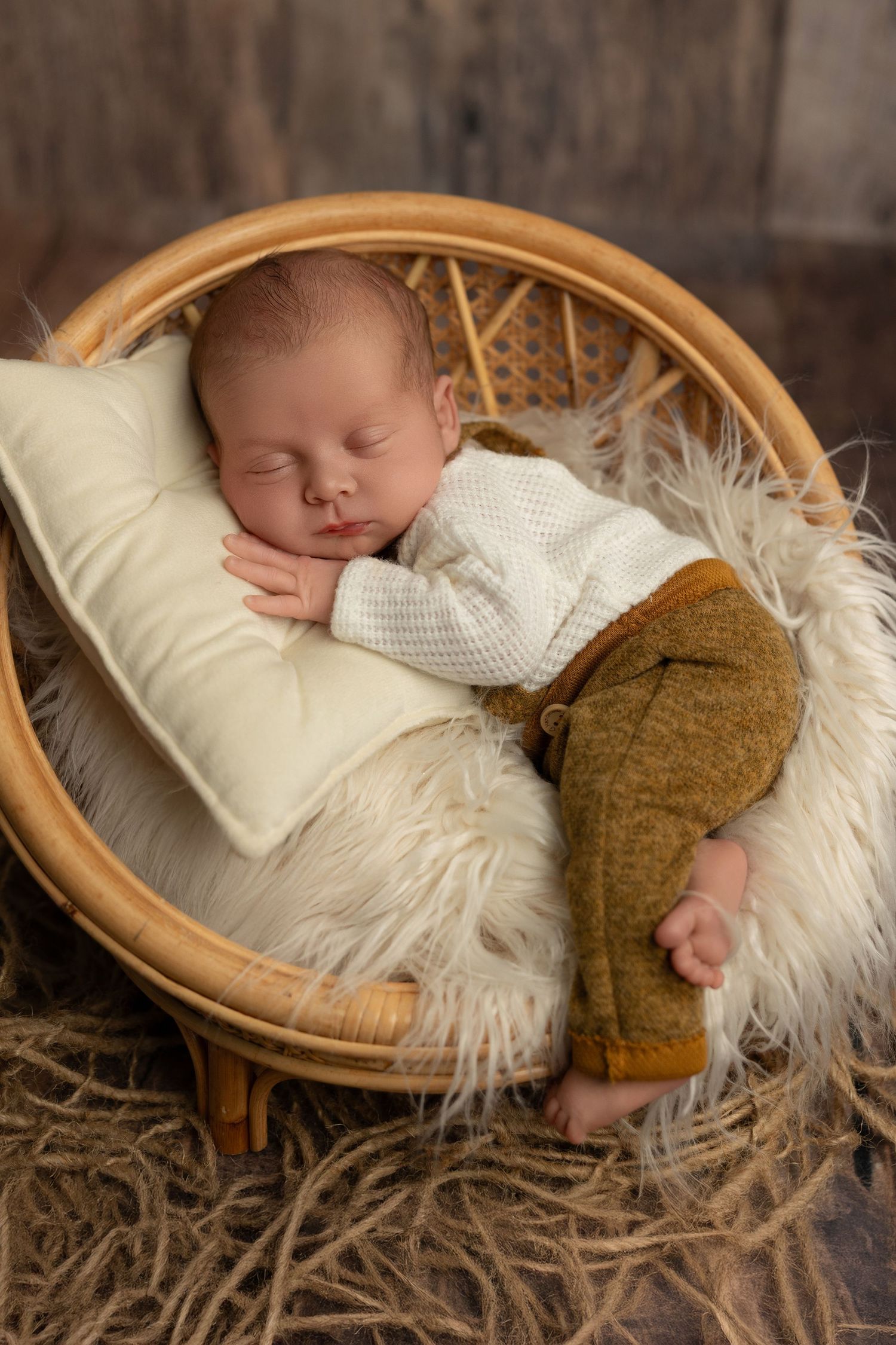 Sleeping baby in white sweater rests peacefully on fluffy white fur inside rattan chair.