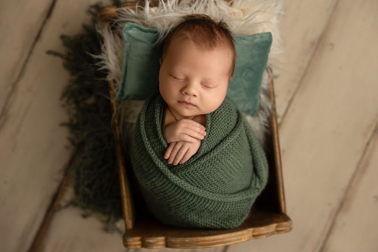A sleeping baby wearing a green knit sweater rests peacefully on a wooden surface.