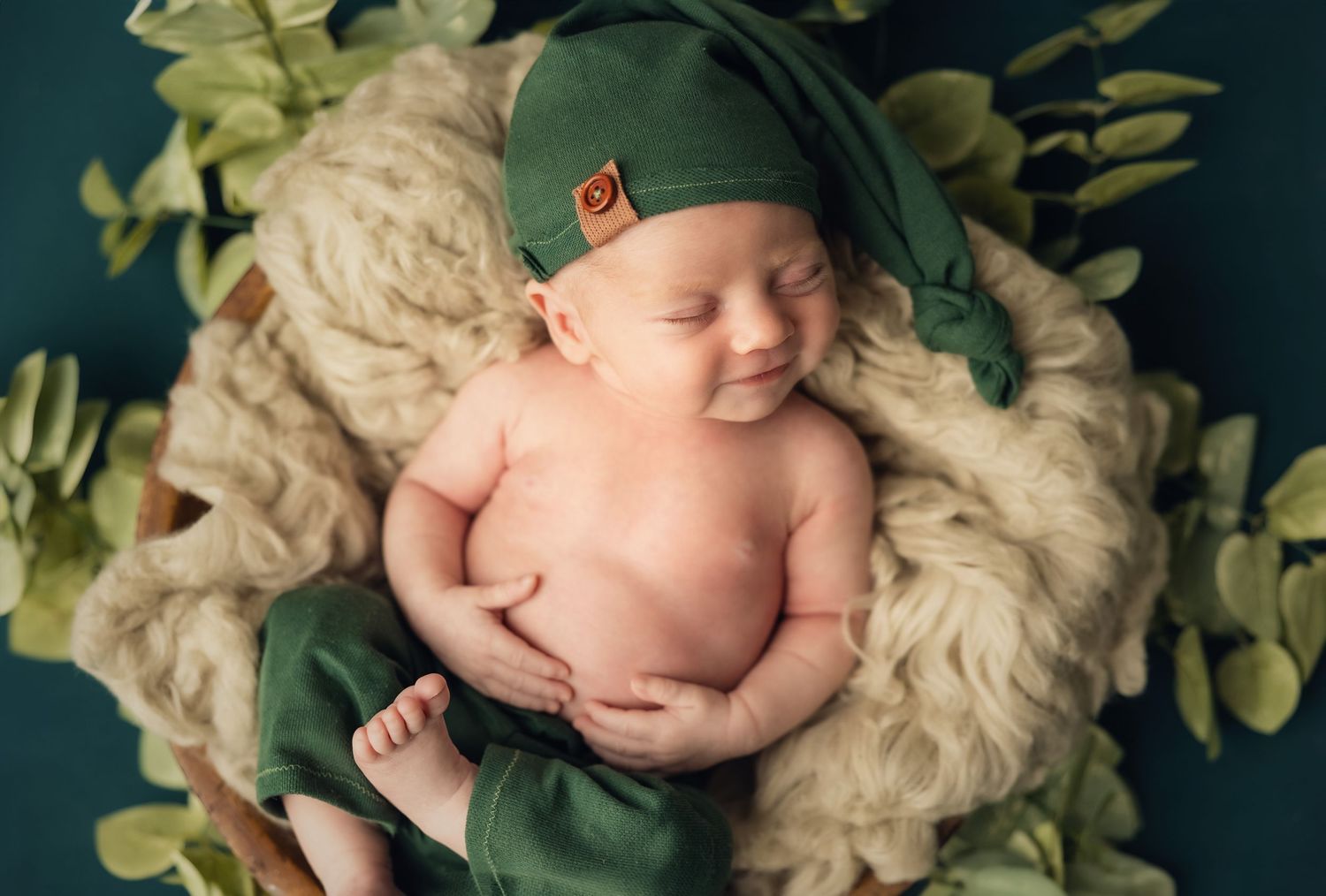 Sleeping newborn baby nestled in white floral arrangement against dark teal background.