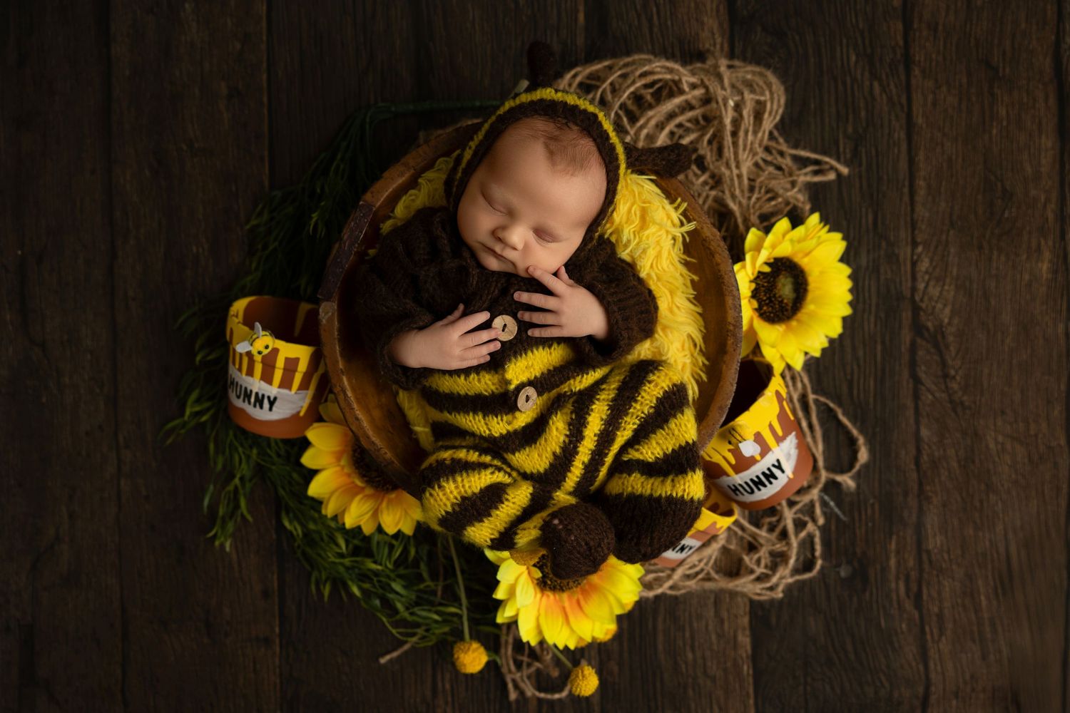 Newborn baby sleeping peacefully in rustic wooden setting with bright yellow sunflowers and burlap accents.