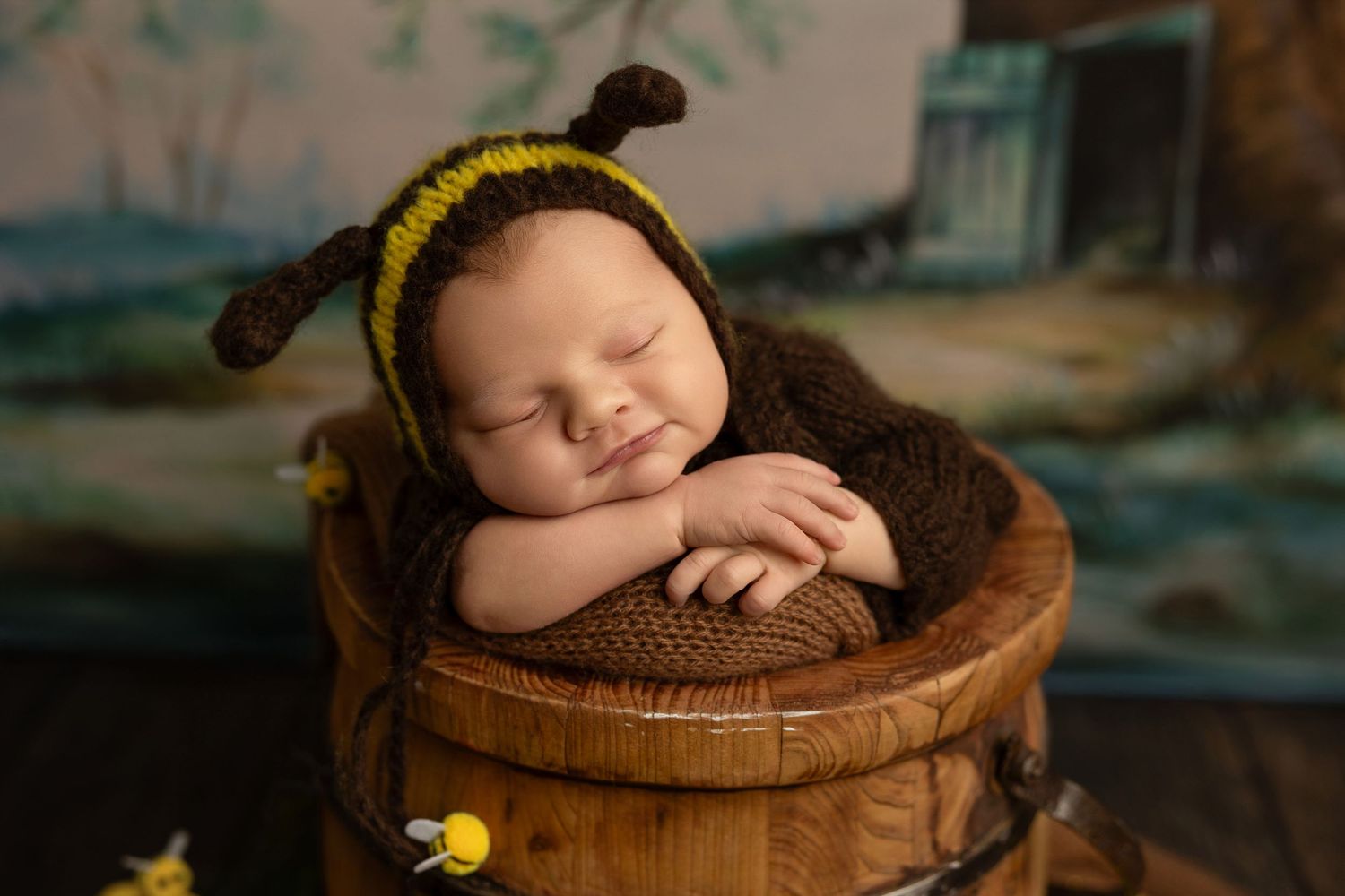 Sleeping baby in brown knit wrap posed in wooden bowl during professional newborn photo session.
