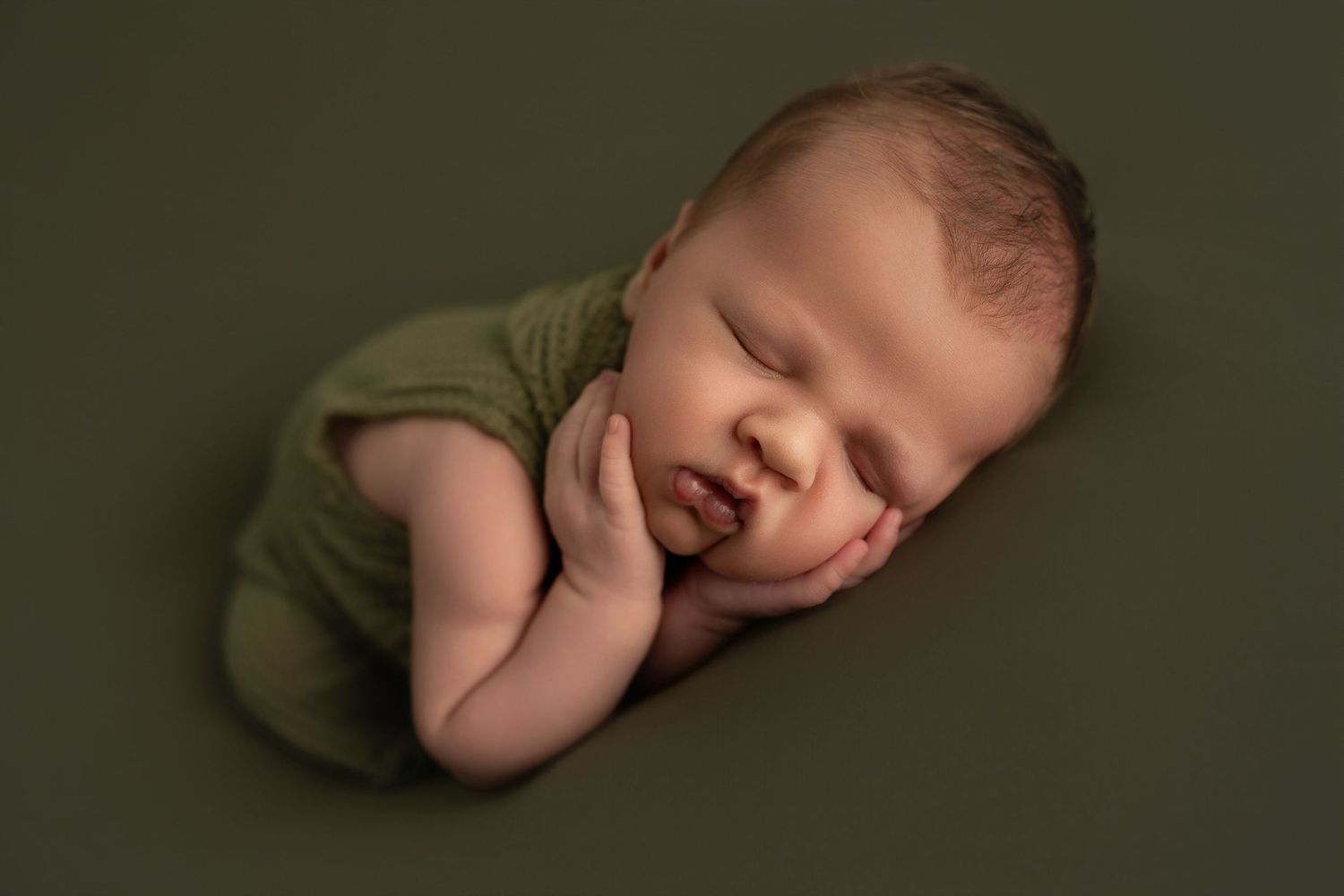 Sleeping newborn baby wearing olive green wrap photographed from different angles in dark moody lighting.