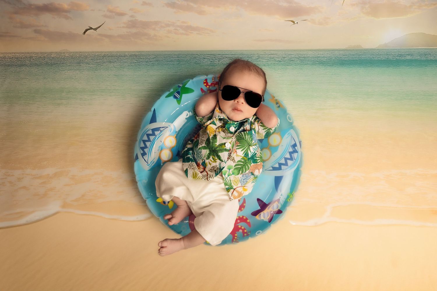 A newborn baby lies on a floral blanket against a soft beige backdrop in a professional studio setting.