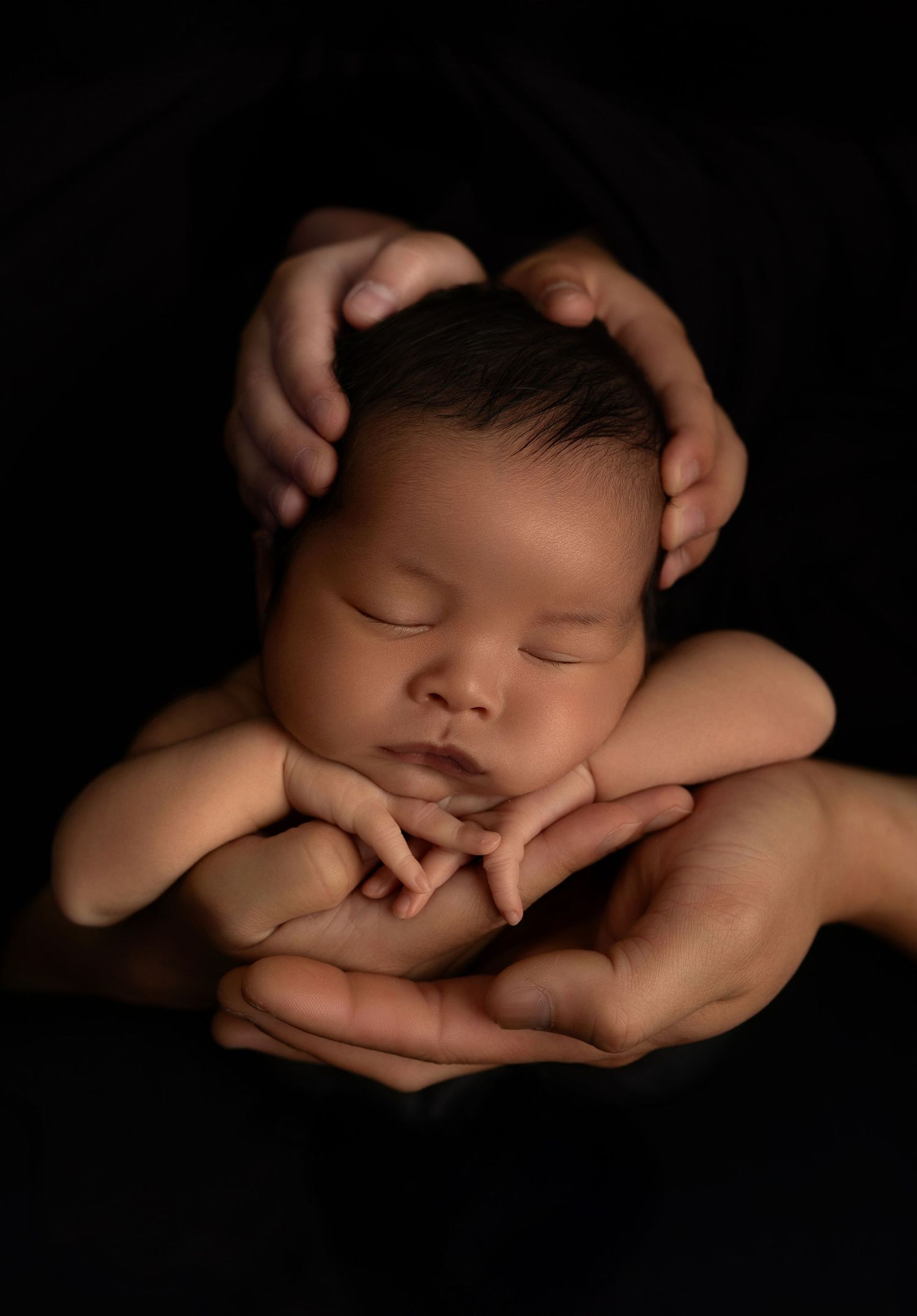 A sleeping newborn baby cradled in gentle hands against a dark background in a series of artistic portraits.