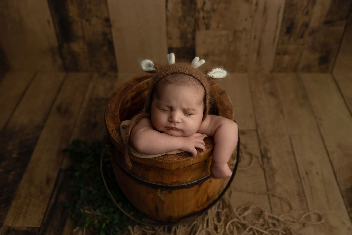 A sleeping baby rests peacefully in a wooden bowl prop during a professional newborn photography session.