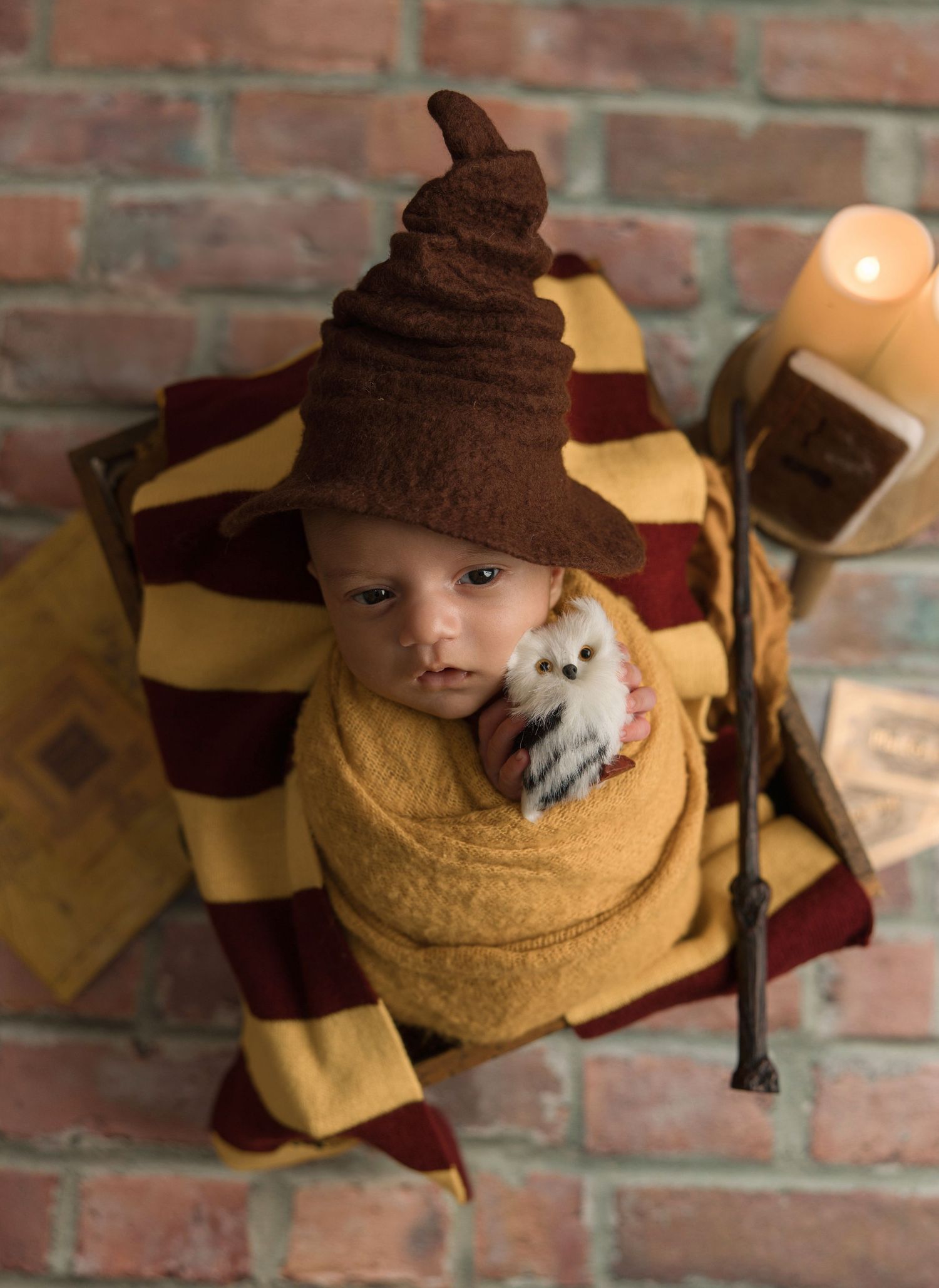 A small dog wearing a brown hat and yellow sweater sits against a brick wall in a cozy autumn outfit.