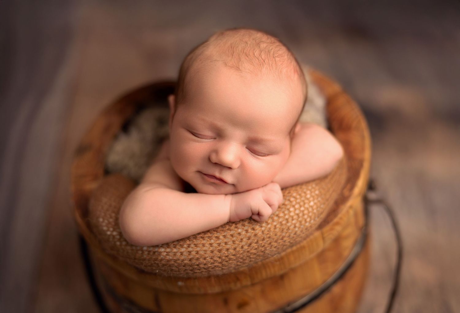 Sleeping newborn peacefully rests in a cozy brown wooden bucket with soft knit blanket.