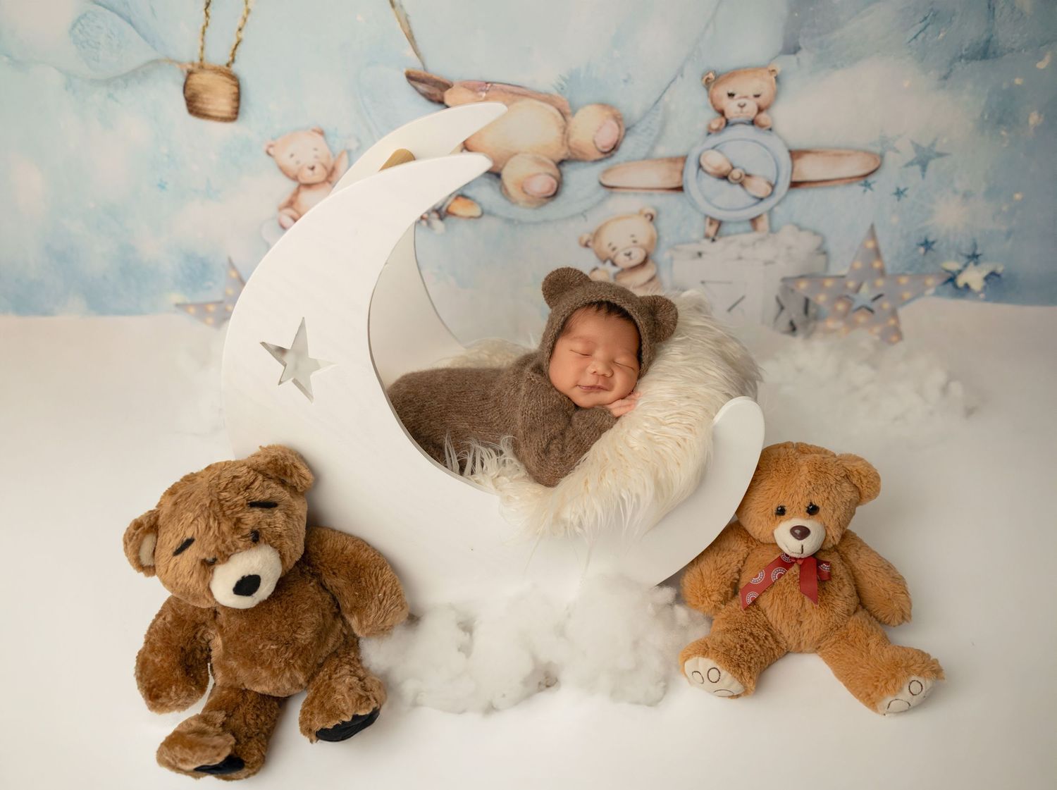 A series of teddy bears and plush toys arranged with a moon prop against a dreamy blue watercolor background.