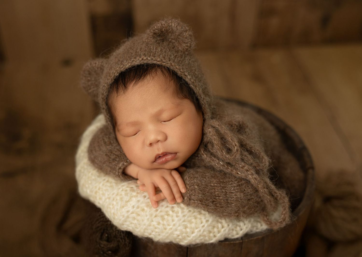 Sleeping newborn baby wrapped in soft brown and cream colored blankets in professional studio photography setting.