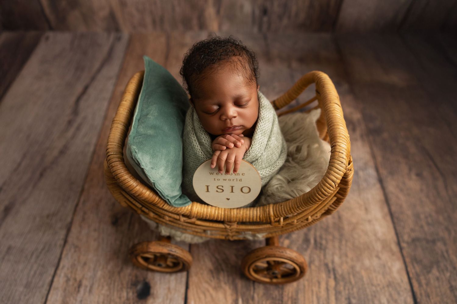 Baby sleeping peacefully in vintage wicker carriage with green cushion on wooden floor.