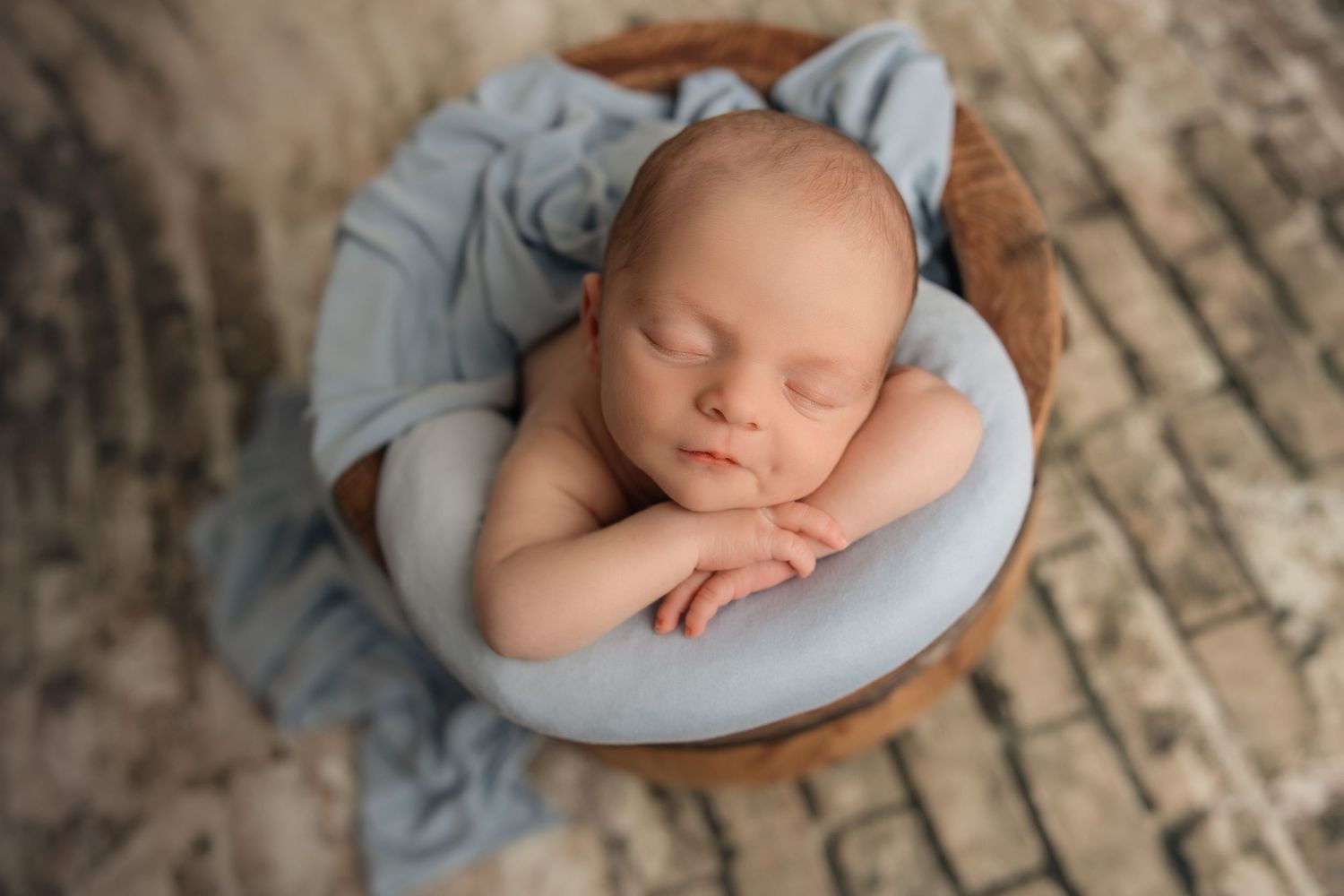 Sleeping newborn baby wrapped in soft blue fabric posed on rustic wooden floor during professional photo session.