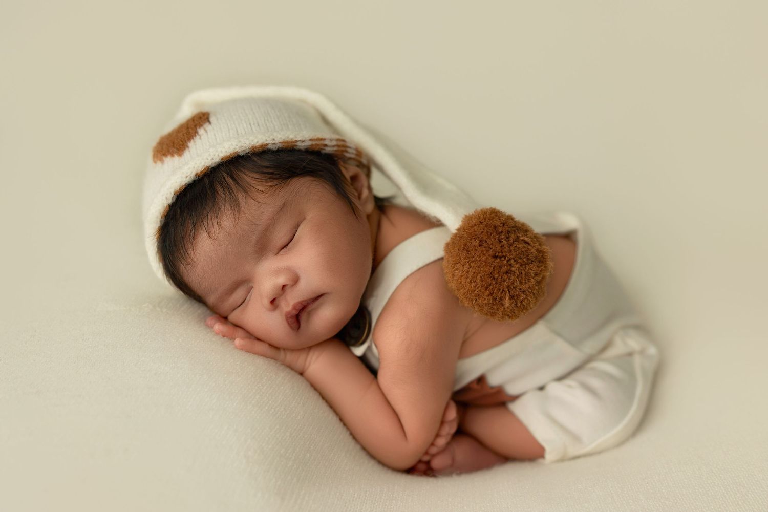 A sleeping baby swaddled in white blankets rests peacefully against a neutral beige background.