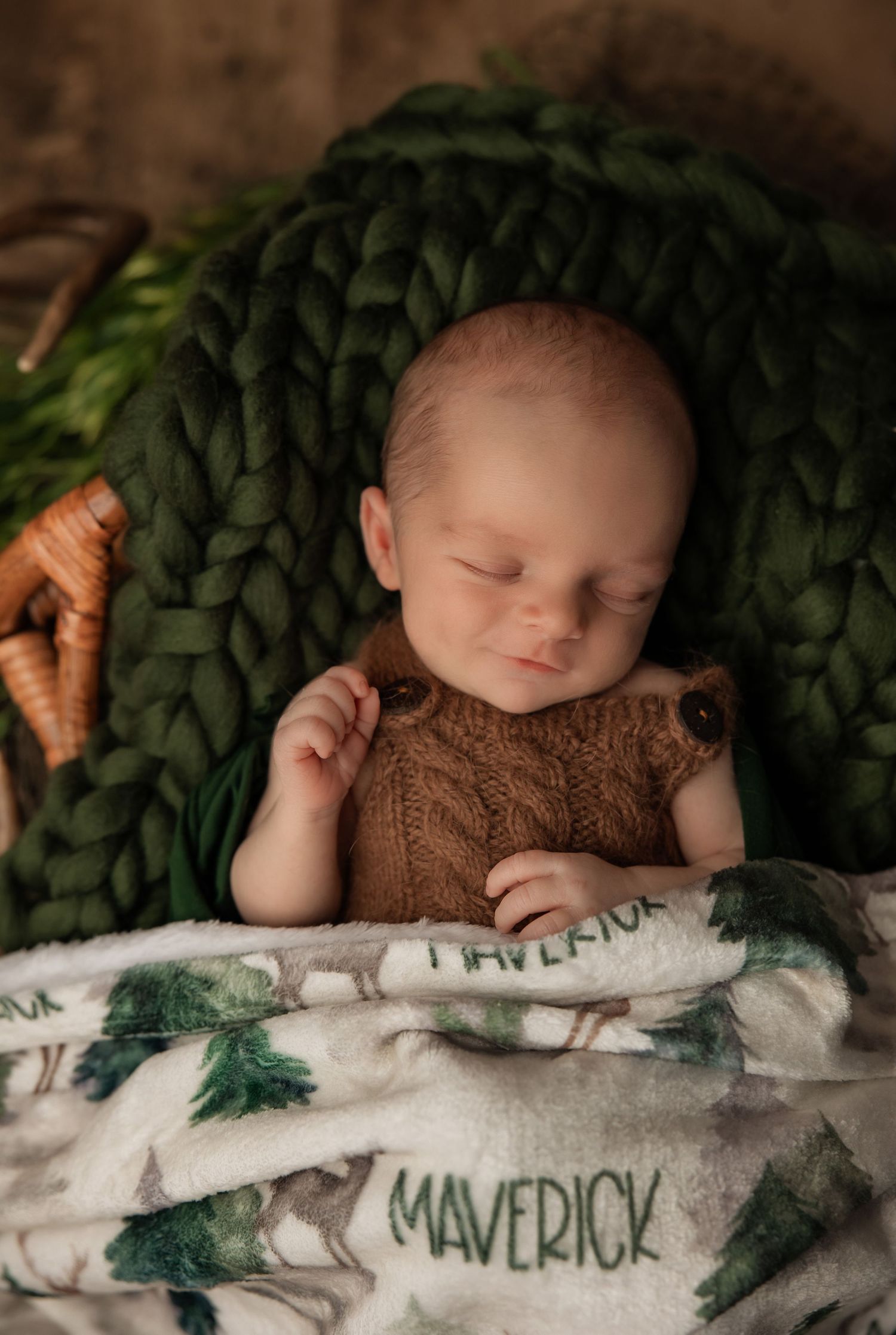 Sleeping baby nestled in green chunky knit blanket with personalized name blanket and brown outfit.
