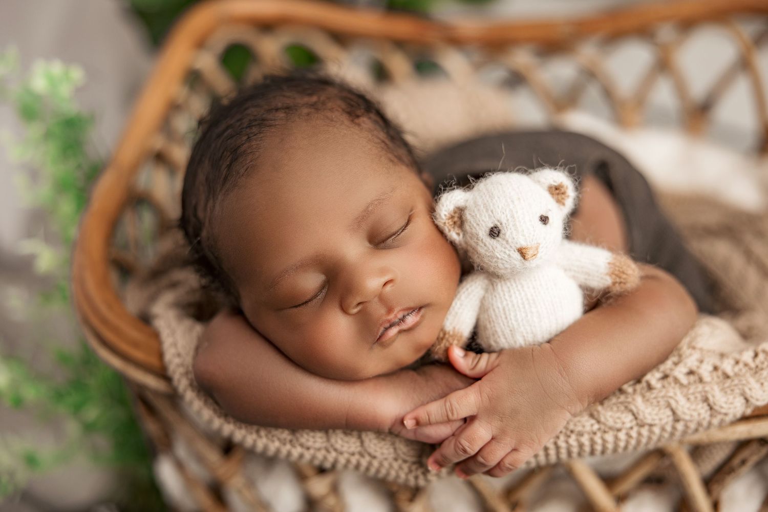 Sleeping baby peacefully cuddled with small white teddy bear on wicker chair.