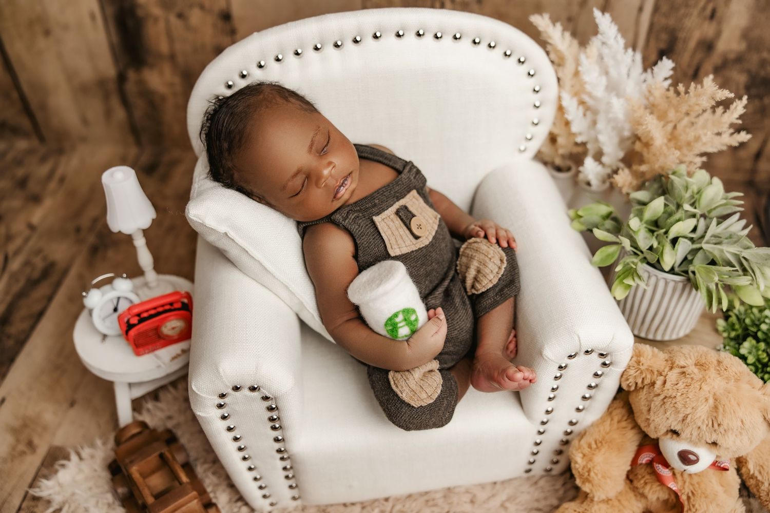 A cozy newborn photography session featuring a tiny baby sleeping on a white miniature bed with plush teddy bears nearby.