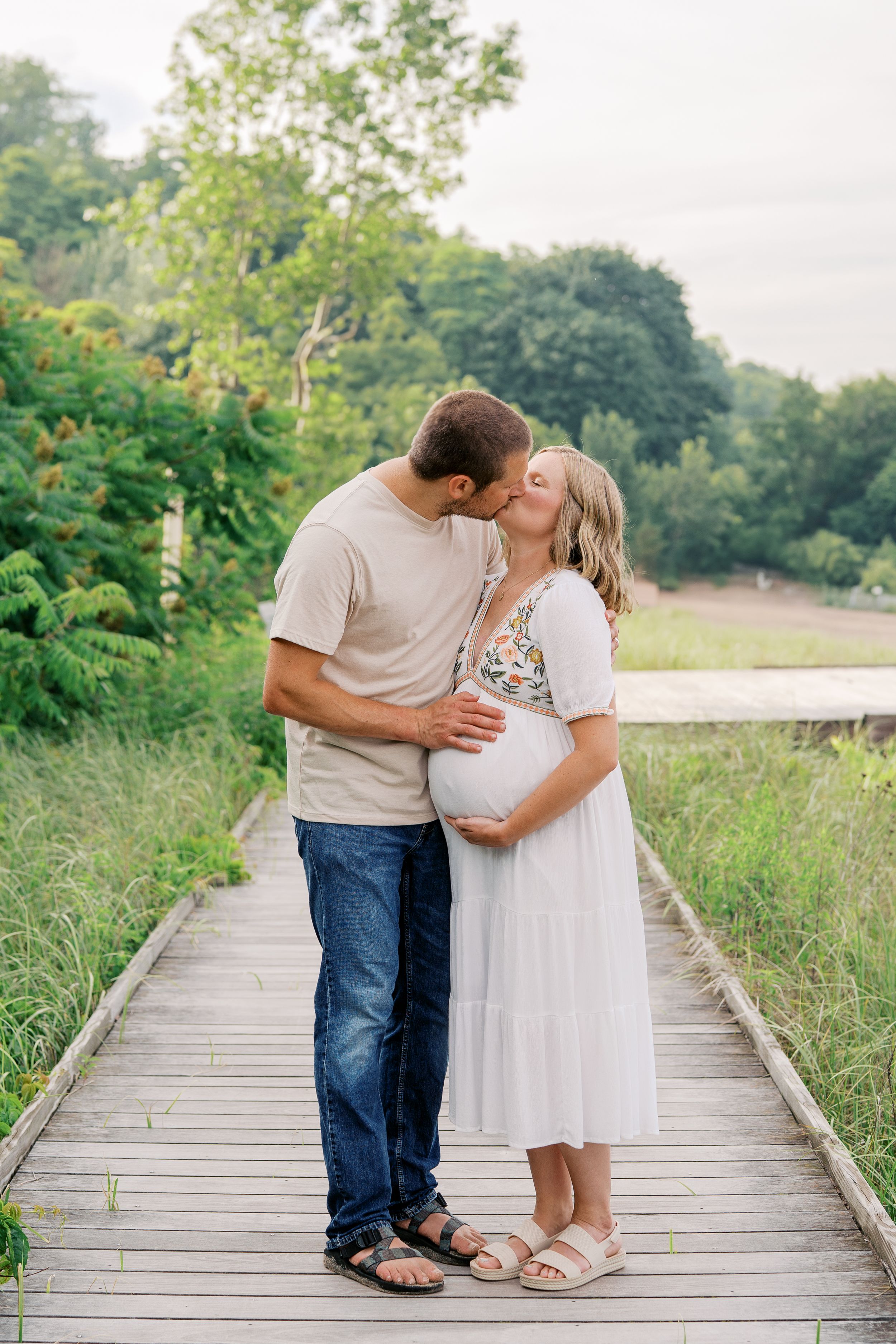 Couple sharing tender moments while walking along a rustic wooden pathway through green summer foliage.