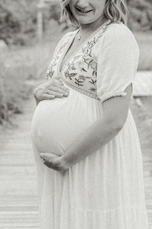 A person in a white floral dress stands outdoors in a black and white photograph.
